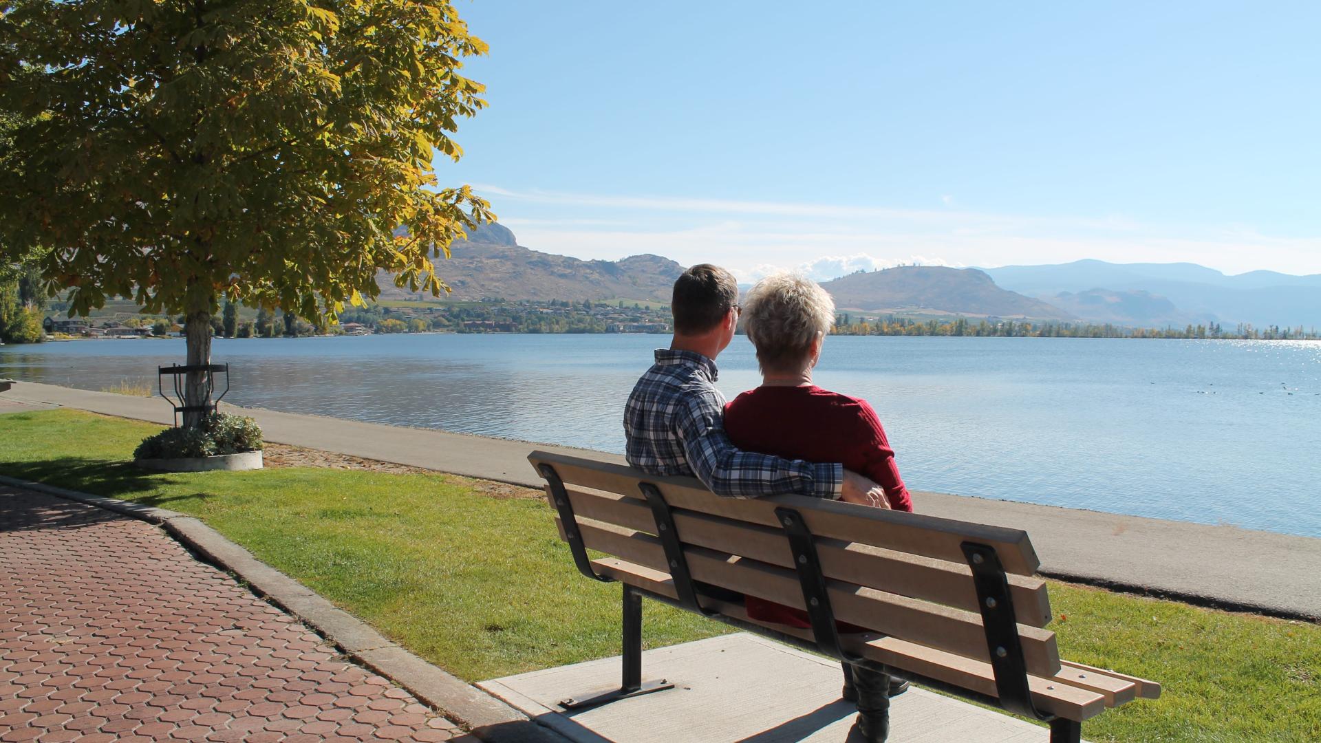 Couple sitting on park bench facing waterfront